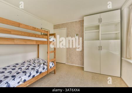 A beautifully designed minimalist bedroom featuring a wooden bunk bed and a sleek white wardrobe, creating a cozy and functional space. Stock Photo