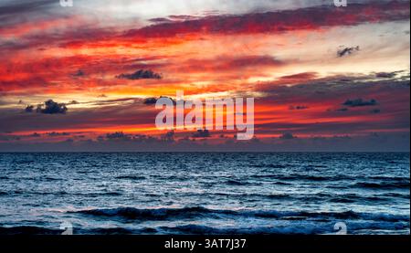 Vibrant sunset over a calm ocean with dramatic red and orange clouds. Stock Photo