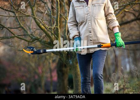 Woman carrying long handled loppers for trimming trees in rural garden. Tree pruner gardening tool Stock Photo