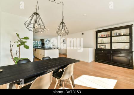A bright and airy dining room featuring a sleek black table and stylish pendant lights. Green plants enhance the modern aesthetic of the interior design. Stock Photo
