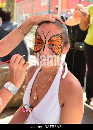 August 10, 2013 - Brooklyn, New York, U.S. - Smiling young woman is having a beautiful orange butterfly air brush painted on her face by volunteer artist Laura Yorburg, during the 3rd Annual Coney Island History Day celebration. (Credit Image: © Ann Parry/ZUMA Wire) Stock Photo