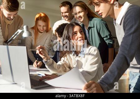 Group of university students collaborating on project and discussing ideas around desk with laptop. Stock Photo