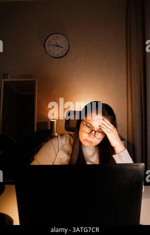Woman working on computer late evening at home office. Concentrated female freelancer trying to solve business problems. Working and suffering from we Stock Photo