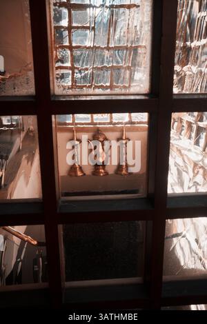 London, UK - September 28, 2024: Warm-toned brass objects viewed through vintage wavy glass panes of a historic window, reflecting light and detail in Stock Photo