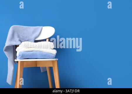 Stack of folded sweaters on chair against blue background Stock Photo