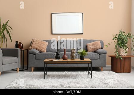 Comfortable grey sofa with soft pillows and blank photo frame hanging on beige wall in living room Stock Photo