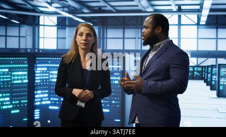 Team of admins in high tech data center looking at hologram visualization. Engineer and coworker working on securing serves using AR tech, preventing hacker attacks, camera A Stock Photo