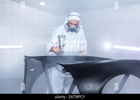 Skilled worker using spray gun to paint car body in workshop. for automotive repair, vehicle customization, or industrial craftsmanship concepts. Stock Photo