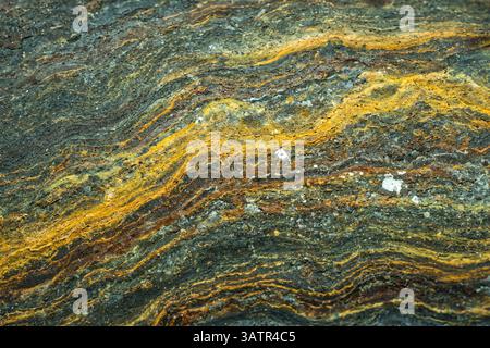 A close-up view of a rock formation with wavy, parallel bands. The primary colors are yellow and dark gray, with scattered white specks. Stock Photo