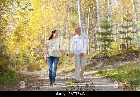 Happy married couple - husband and his pregnant wife walk in autumn forest Stock Photo