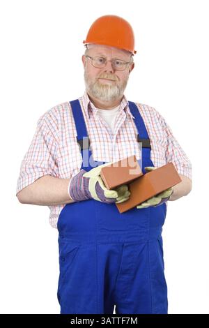 Bricklayer in blue dungarees and helmet holds bricks in his hand Stock Photo