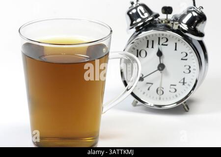 Cup with herbal tea and alarm clock against a white background Stock Photo