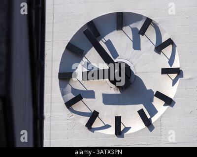 A close-up of a modern, minimalist clock with black hands and hour markers on a white wall in Basel Stock Photo
