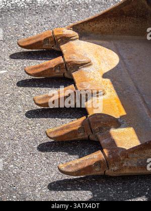 Close-up of a rusty excavator bucket with metal teeth on an asphalt surface. Stock Photo