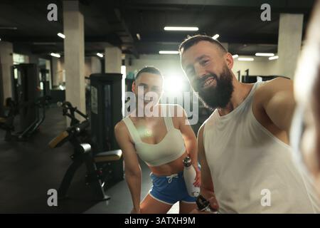 Couple with water bottles taking selfie after training in gym Stock Photo