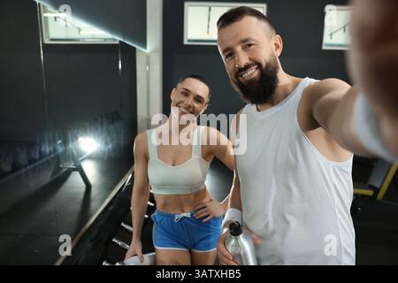 Couple with water bottles taking selfie after training in gym Stock Photo