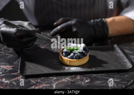 Confectioner decorating tasty tart with mint at dark table, closeup Stock Photo