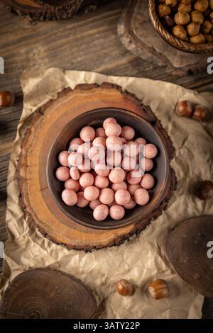 Bowl of raspberry flavour white chocolate covered hazelnuts on rustic background Stock Photo