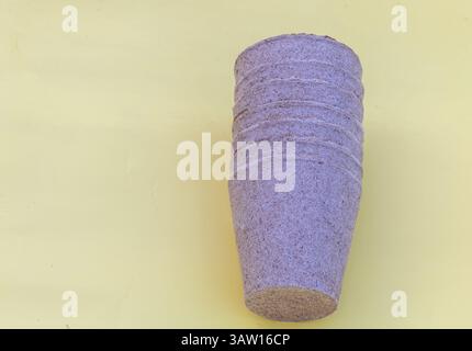 a purple pear on a solid yellow background, a long shot of one round biodegradable pulp origami pot made from textured wood material and plant fibers Stock Photo