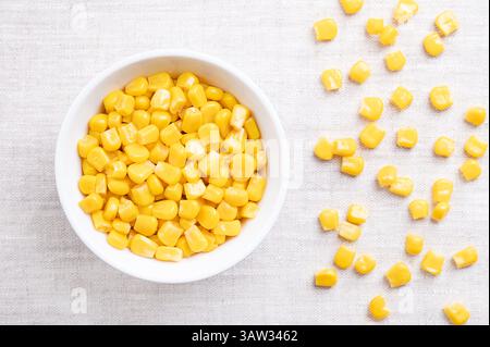 Canned vegetable maize, whole sweet corn kernels in a white bowl on linen. Variety of corn that is picked when in its milk state. Clean, sound kernels Stock Photo