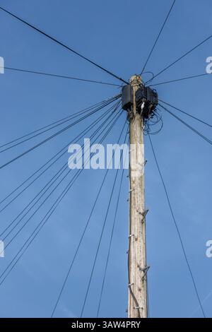 Wooden pole with modern telecoms equipment and multiple wires forming a star pattern from the top of the pole set against a clear blue sky background Stock Photo