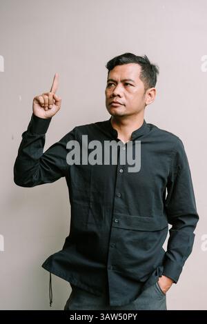 An asian man points upward, possibly representing a solution or inspiration, copy space available Stock Photo