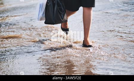 Businesswoman with handbag wading through a flooded street after heavy rain, facing difficulties on her way to work Stock Photo
