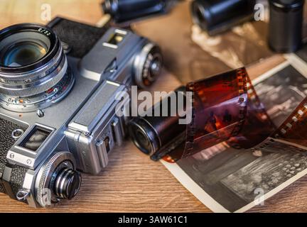 A vintage camera rests on a wooden surface surrounded by black and white photographs and film rolls, evoking nostalgia for classic photography. Stock Photo