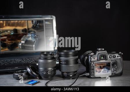 Different camera lenses and gear are arranged next to a laptop displaying editing software in a cozy workspace, ideal for photographers. Stock Photo
