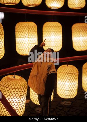 Boy Pointing at Illuminated Paper Lanterns at Night during a nighttime festival in the heart of a bustling city Stock Photo