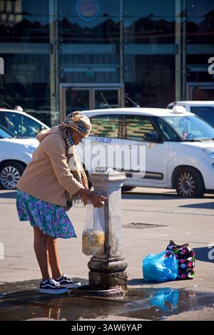 Woman washing raw peanuts  in their shells - monkey nuts - in a bag at a water fountain in central Naples, Italy.  Monkey nut is a term used in the UK. They use the term to describe a raw peanut in the shell Stock Photo