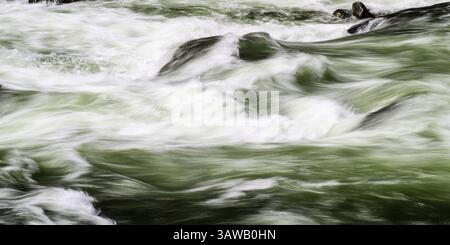 River rages in whitewater shapes in long exposure with green waves Stock Photo