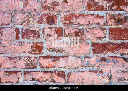 Faded cracked pink paint peeling from red brick wall in closeup Stock Photo