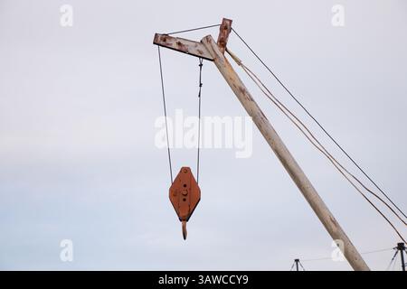 Old crane with metal hook against blue sky in the daytime outdoors Stock Photo
