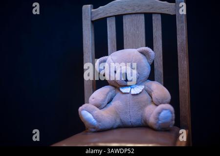 Soft teddy bear on an old wooden chair with plain black background Stock Photo