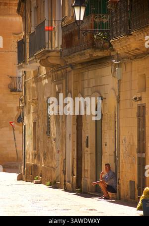 Italian man sitting on the steps to a house, in the street in Lecce, Puglia, Italy Stock Photo