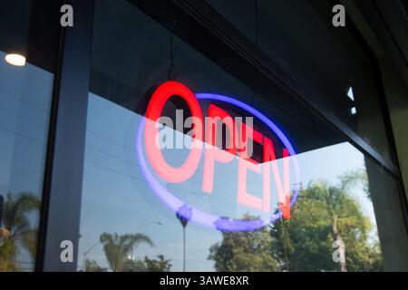 A view of a restaurant front window, featuring the a neon open sign. Stock Photo