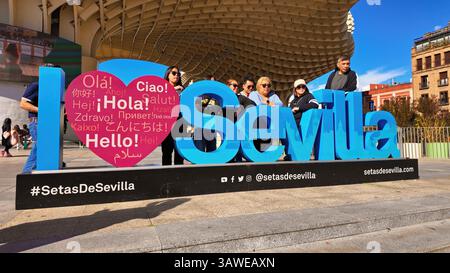 Group of tourists posing at the Setas de Sevilla sculpture with a heart with greetings in different languages and the word Seville - SEVILLE, SPAIN - Stock Photo