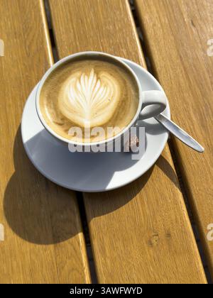 Coffee drink Cappuccino Cappuccio with flower pattern in milk foam, next to it single roasted candied almond on rustic table of outdoor cafe, interna Stock Photo