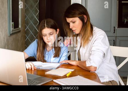 Preteen girl doing homework with mom at home. Mother explaining difficult school subject to her daughter. Spending quality time with child. Happy fami Stock Photo