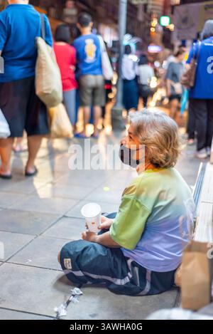Bangkok,Thailand-July 04 2024: Passengers wait for night buses and occasionally give money, on the busy early evening city streets. Stock Photo