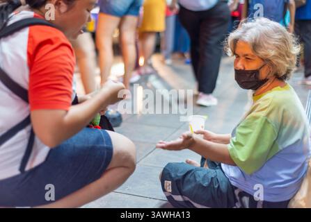 Bangkok,Thailand-July 04 2024: Passengers wait for night buses and occasionally give money, on the busy early evening city streets. Stock Photo