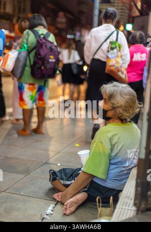 Bangkok,Thailand-July 04 2024: Passengers wait for night buses and occasionally give money, on the busy early evening city streets. Stock Photo