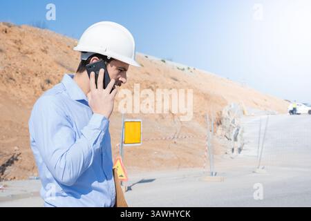A Construction Manager is engaged in a phone discussion at an active construction site Stock Photo