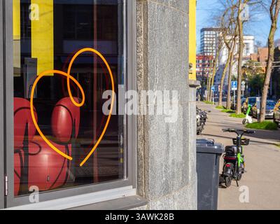 Zurich, Switzerland - April 10, 2025: A bright orange heart-shaped neon sign on a window with a red chair inside, urban street view outside with bicyc Stock Photo