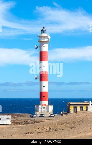 A red and white striped lighthouse stands on a rocky coastline with a blue sky and ocean in the background punta abona tenerife canary islands spain Stock Photo