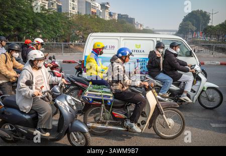 A man driving a motorcycle looks at his mobile phone among motorcycle traffic on a bridge over To Lich river, Cau Giay, Hanoi, Vietnam Stock Photo