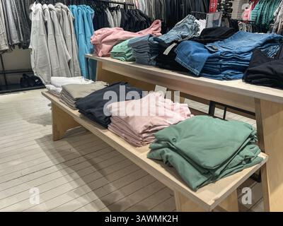 Neatly folded pastel and neutral-colored t-shirts with stacked denim jeans arranged on wooden tables inside a modern retail fashion store, showcasing Stock Photo