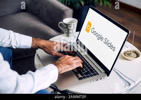 Man using a laptop computer displaying logo of Google Slides on the screen. Slides is a presentation online app. ROSARIO, ARGENTINA - APRIL 20, 2025. Stock Photo