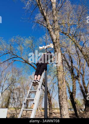 Worker installing security cameras and megaphone on lamp post. Stock Photo